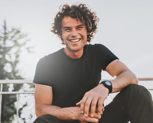 Young man with curly hair grinning outdoors on sunny day