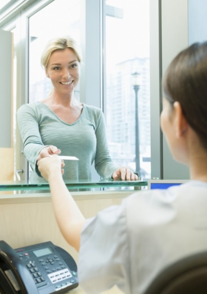 Woman handing payment card to dental team member at front desk