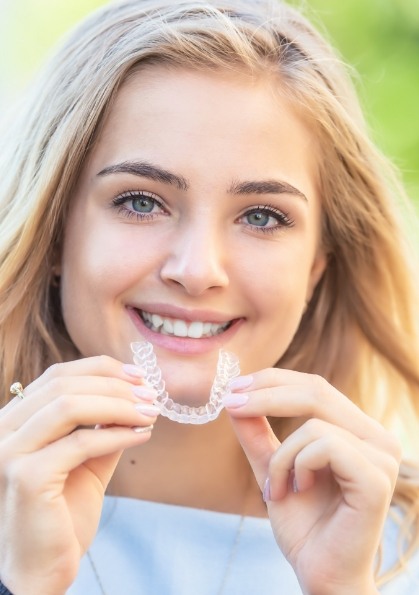 Smiling young woman holding Invisalign aligner outdoors