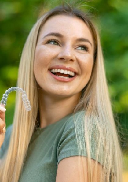 a woman smiling while holding Colgate© aligners