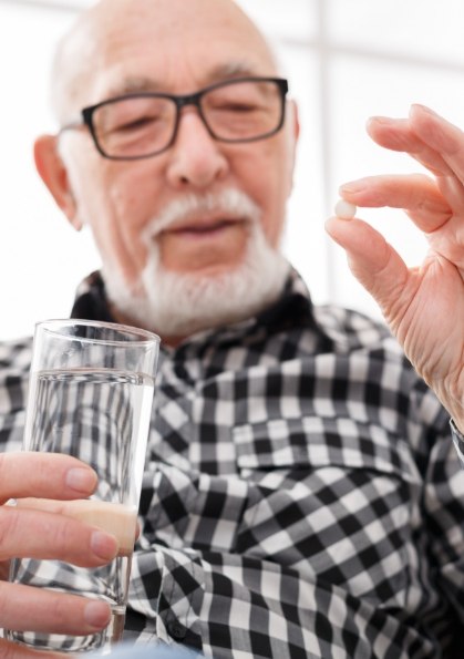 Senior man holding a white pill and a glass of water